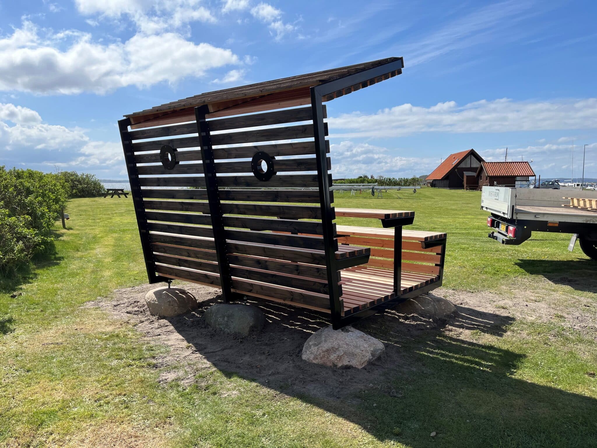 Bagsiden af den halvåbne overdækning af bordbænkesæt. Sortmalet ubehandlet douglas