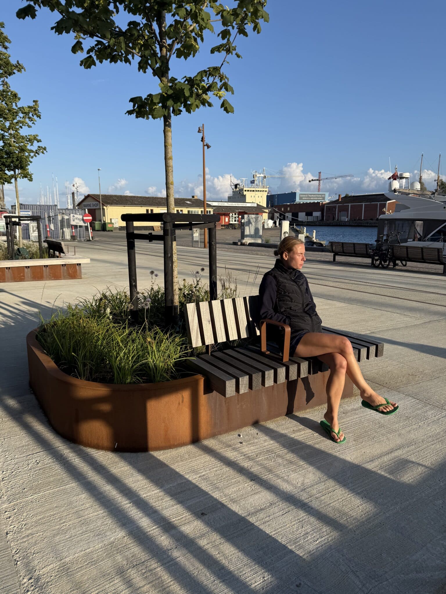 cecilie sidder på indbygget bænk ved plantekasse af corten stål ved svendborg havn
